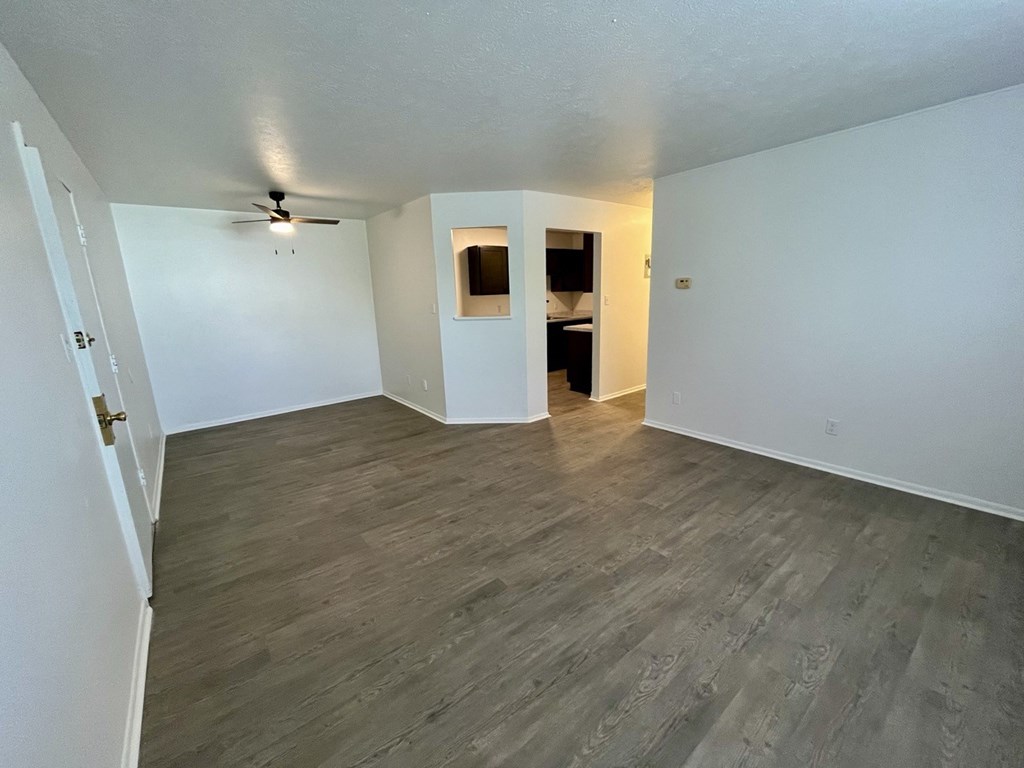 an empty living room with plank flooring and a ceiling fan