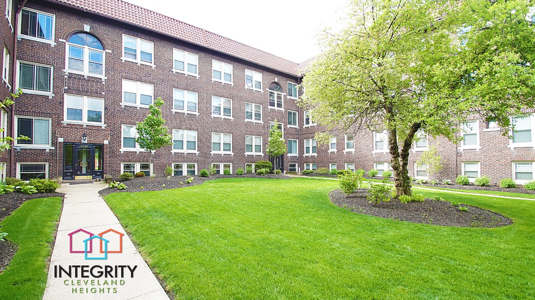 an exterior view of an apartment building with a lawn and tree