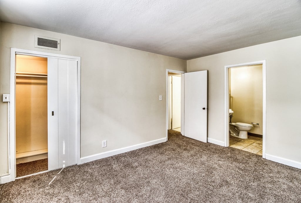 an empty living room with doors to a bathroom and a toilet