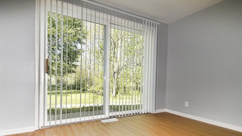 an empty living room with a large window with white vertical blinds