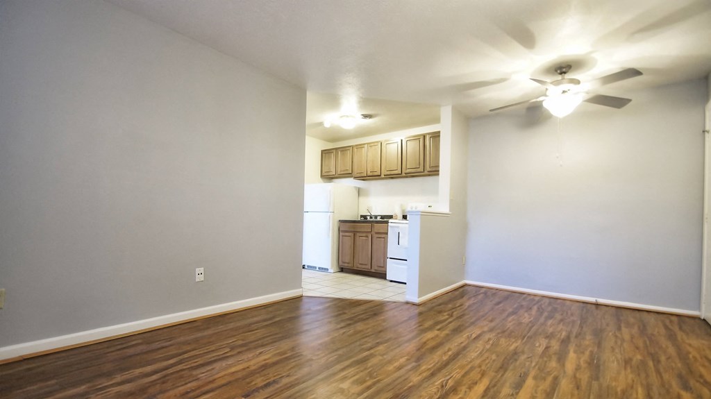 an empty living room and kitchen with wood flooring and a ceiling fan