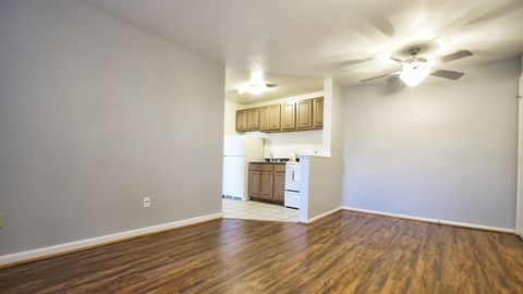 an empty living room and kitchen with wood flooring and a ceiling fan