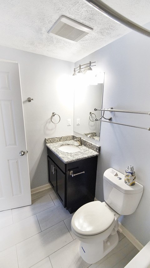A white toilet with a black counter top and a white sink with a black counter top.