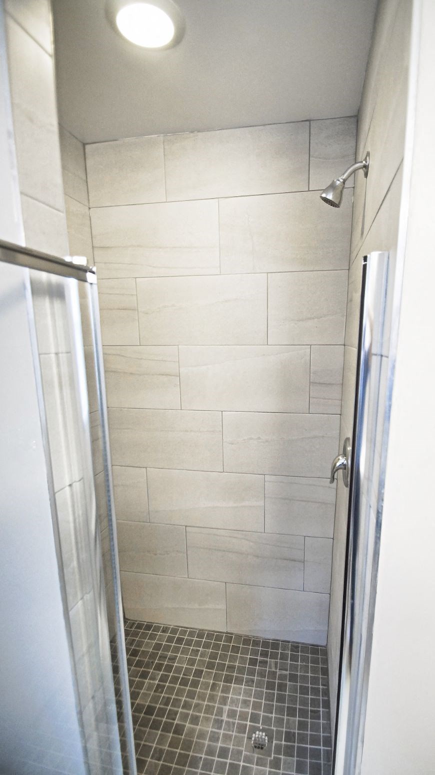 a white tiled bathroom with a shower and a glass door