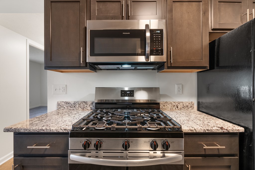A black stove top oven with four burners and a stainless steel microwave above it at Integrity Medina Apartments, OH, 44256
