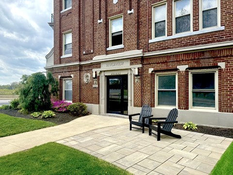 Two black chairs are on a patio in front of a brick building.