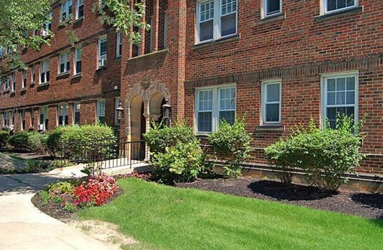 the front of a red brick building with a lawn and bushes