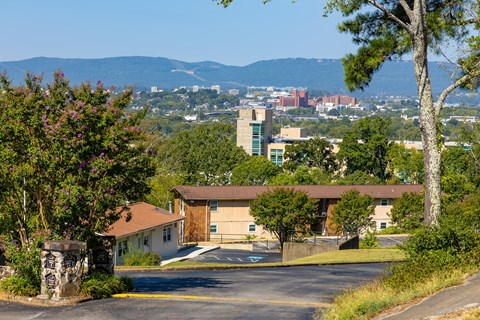 A building with a brown roof is surrounded by greenery and a parking lot.