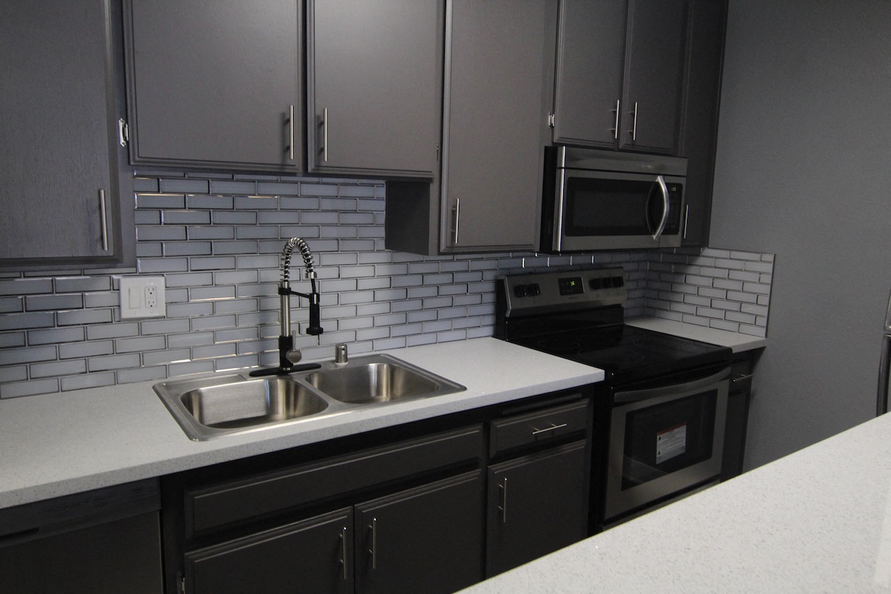 White tiled kitchen with stainless steel fridge, microwave, and oven.