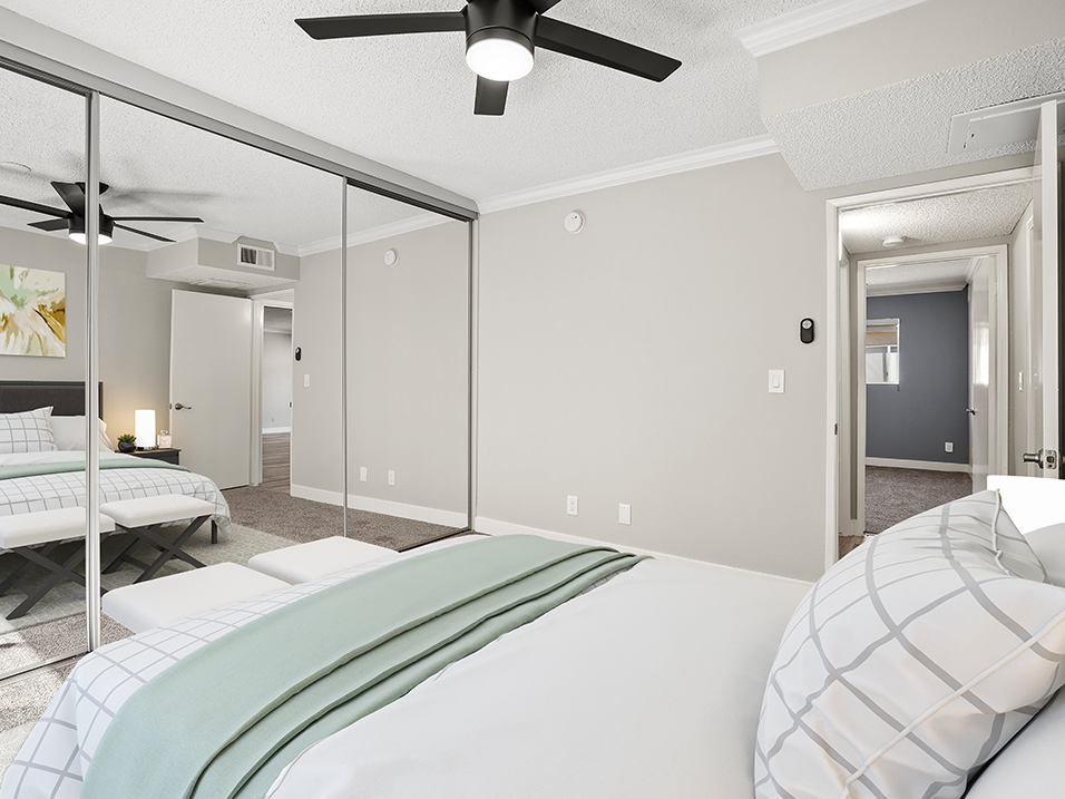 Carpeted bedroom with ceiling fan and large mirrored closet.