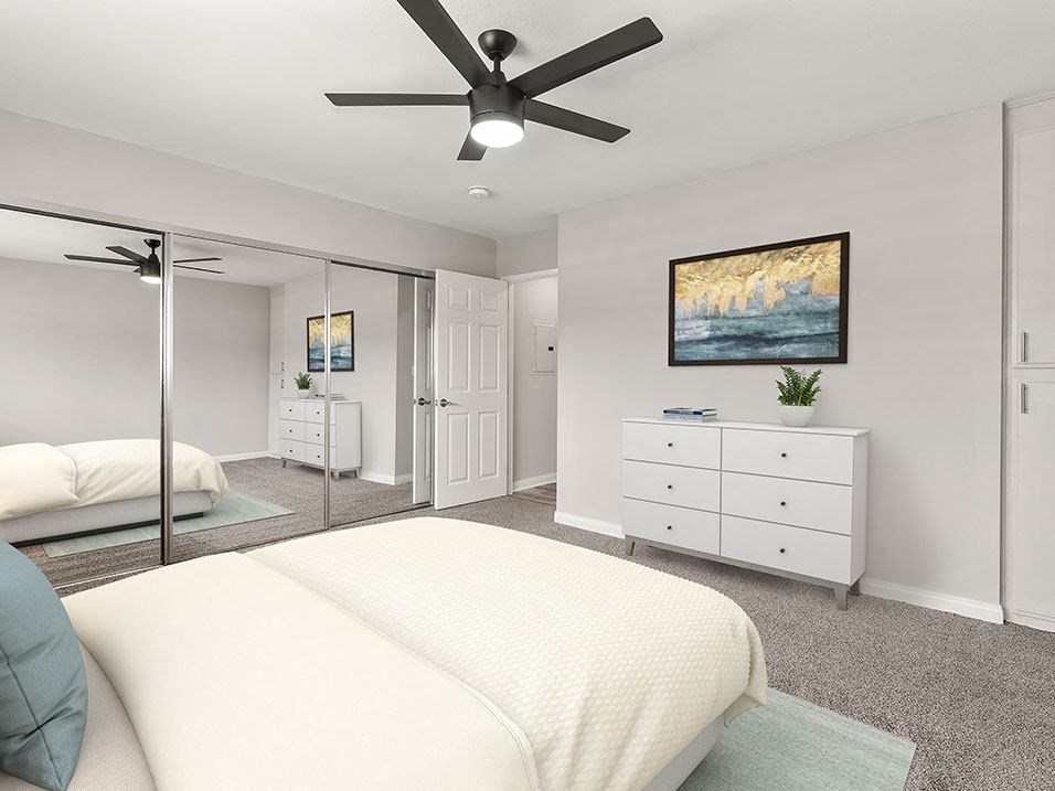 Carpeted bedroom with large mirrored closet and ceiling fan.