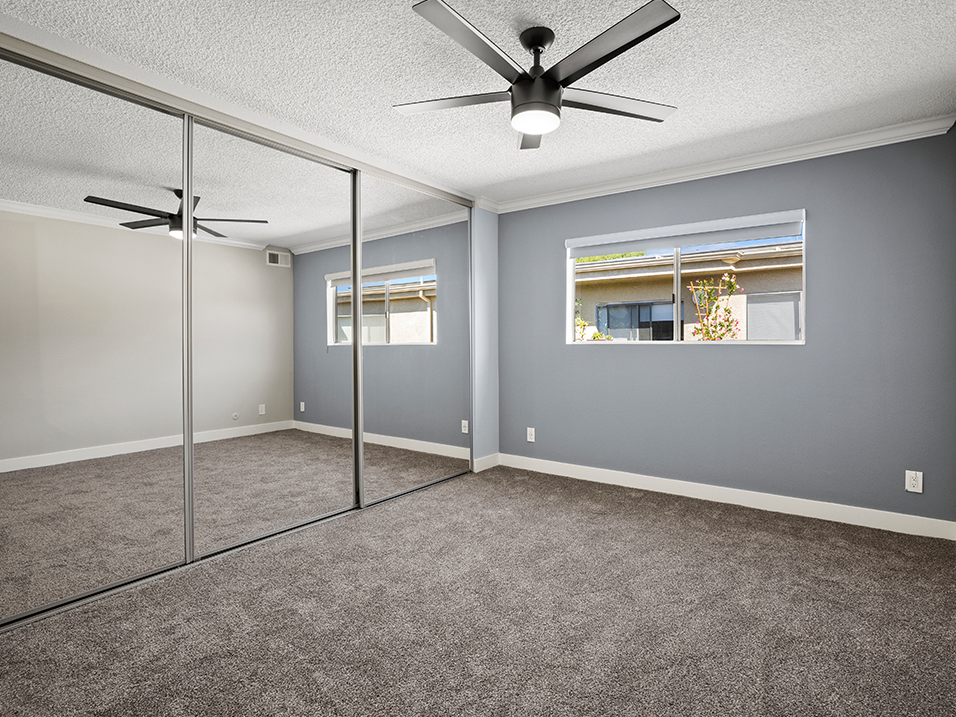 Carpeted bedroom with ceiling fan and large mirrored closet.