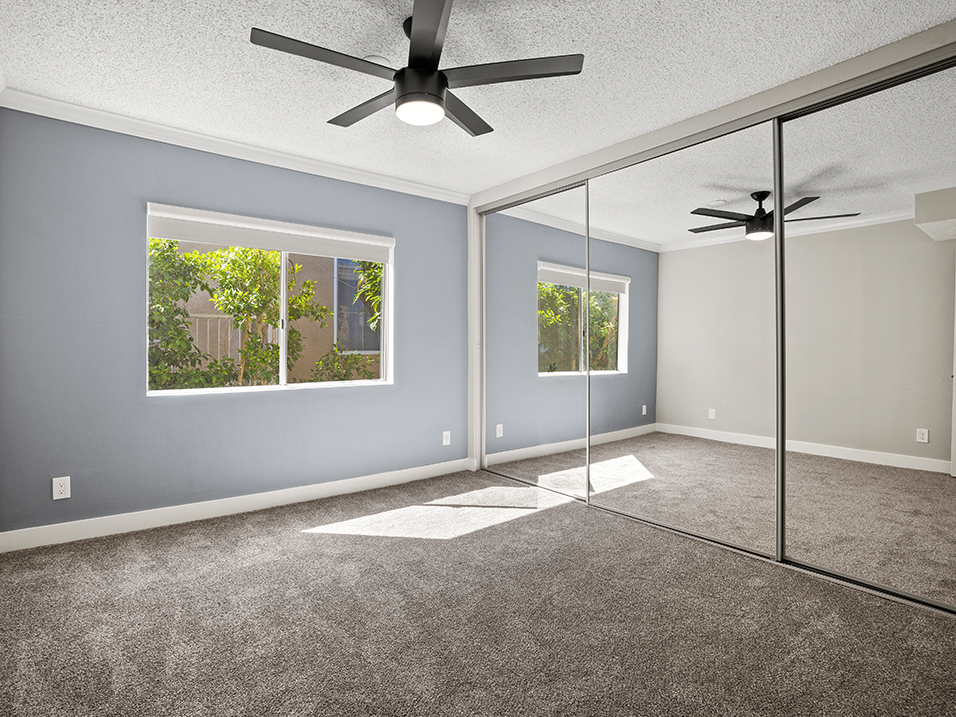 Carpeted bedroom with ceiling fan and large mirrored closet.