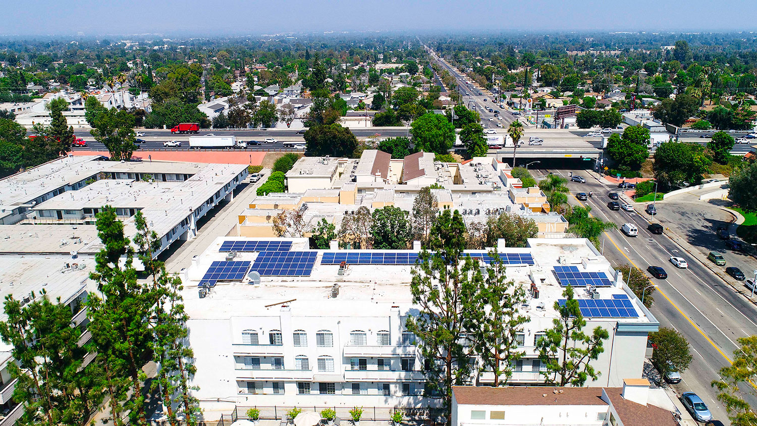 Aerial drone view of Chateau Encino showing energy-efficient white roof, solar panels, and access to 101 freeway.