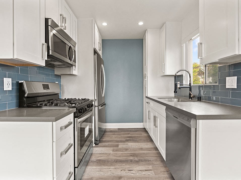 Blue tiled kitchen with stainless steel oven, microwave, and fridge.
