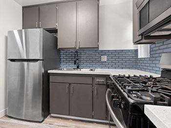 Blue tiled kitchen with stainless steel fridge, oven, and microwave.