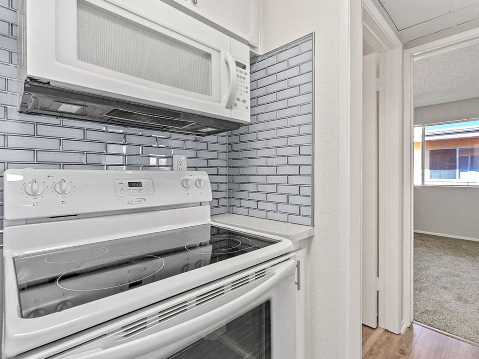 White tiled kitchen with stainless steel oven and microwave.