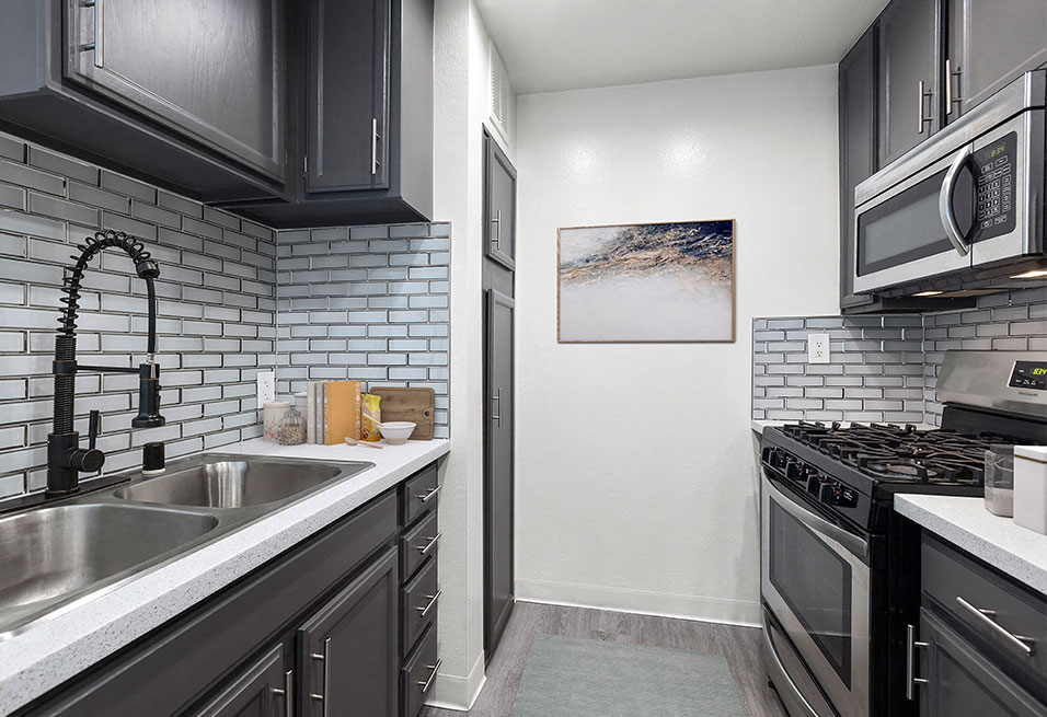 White tiled kitchen with stainless steel fridge, oven, microwave, and fixtures.
