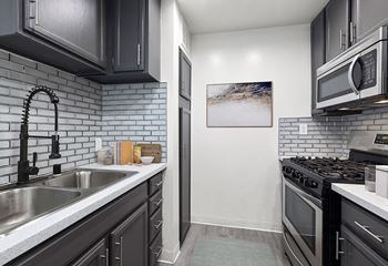 White tiled kitchen with stainless steel fridge, oven, microwave, and fixtures.