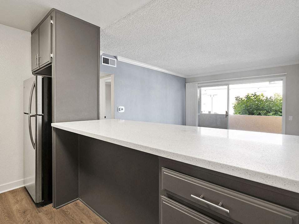 White tiled kitchen with bar seating facing hardwood floored living room.