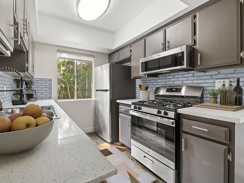 Tiled kitchen with stainless steel oven, microwave, and fridge. - Photo Gallery 1