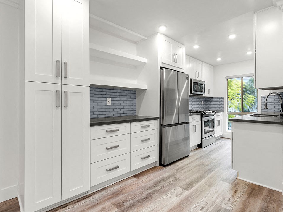 Blue tiled kitchen with stainless steel fridge, oven, and microwave.