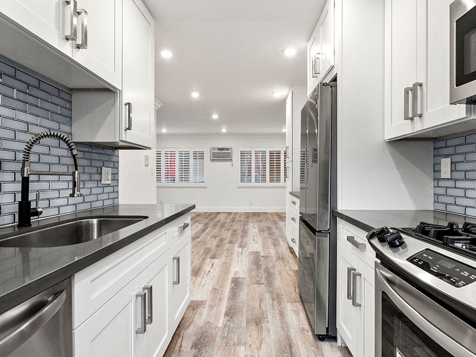 Glass tiled kitchen with stainless steel appliances and view of spacious living room.