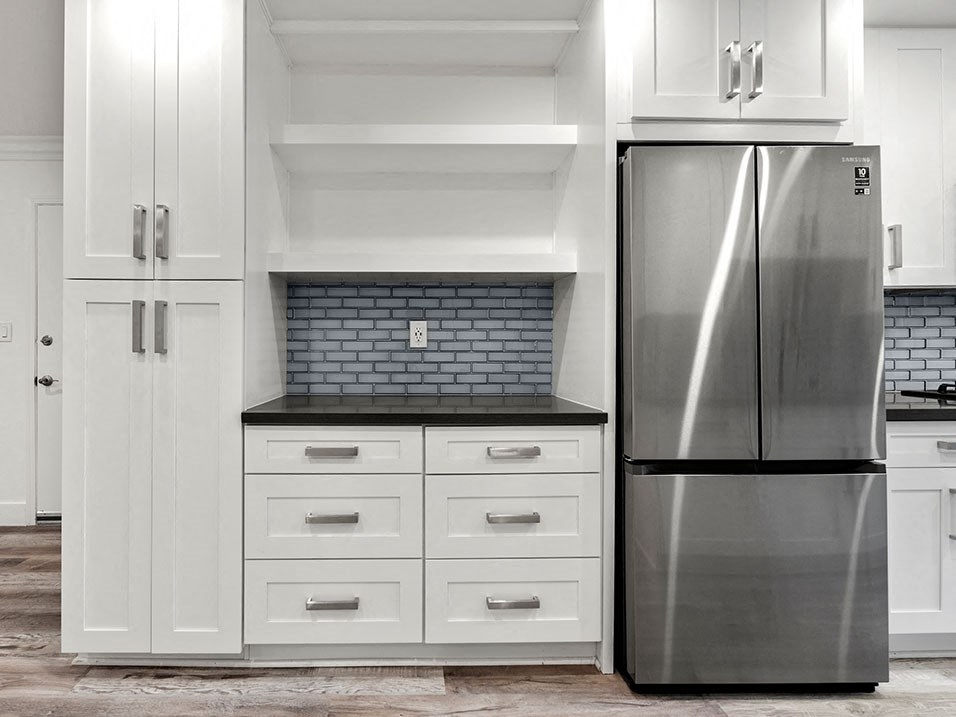 Stainless steel fridge adjacent shelving and storage cabinetry.