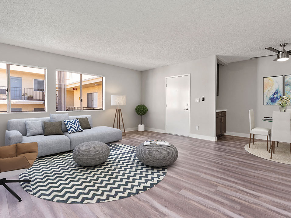 A living room with a grey sofa, a black and white rug, a grey ottoman, a dining table with chairs, and a ceiling fan.