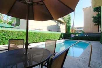A table with chairs and an umbrella is in front of a pool.