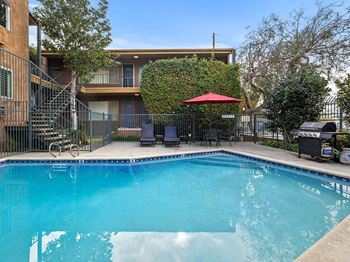 A swimming pool in a backyard with a red umbrella and a building in the background.