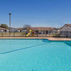 a large swimming pool with a fence and houses in the background