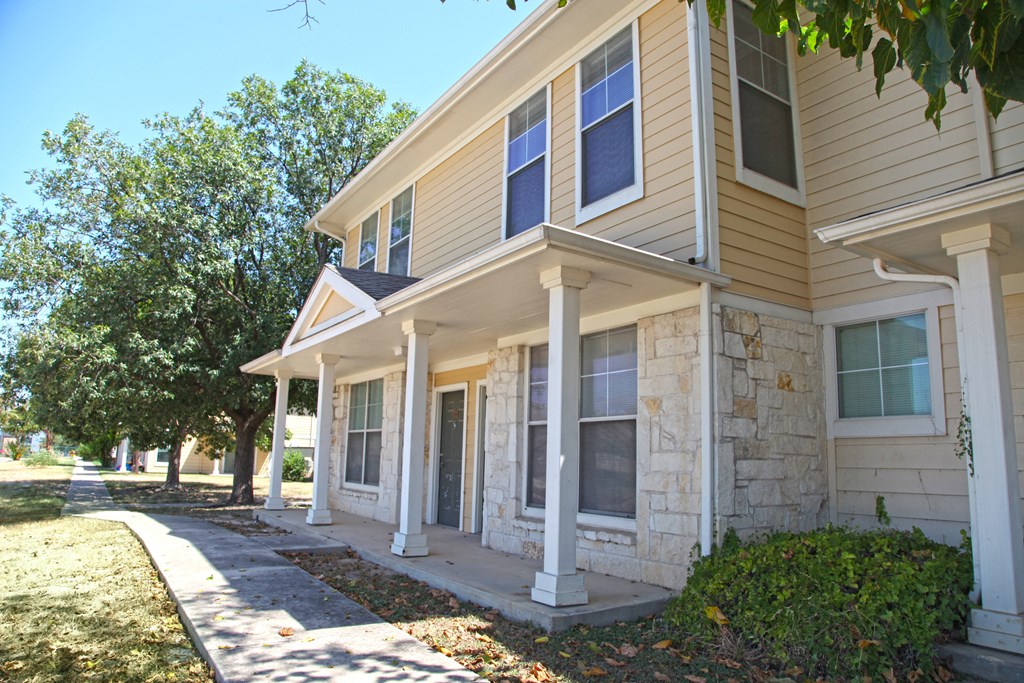 a white and tan house with trees and a sidewalk