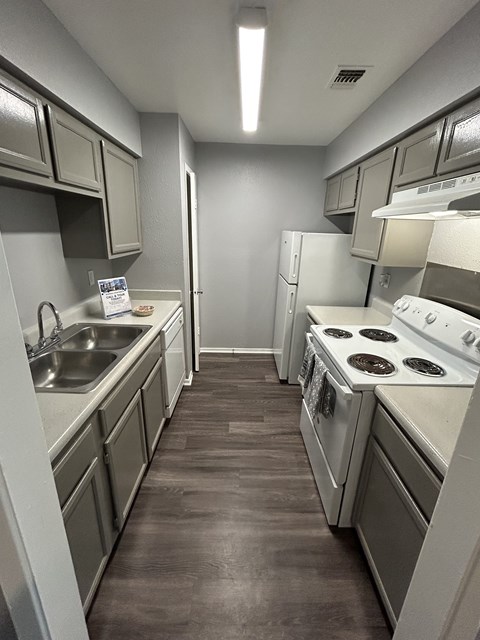 A kitchen with white appliances and a brown floor.