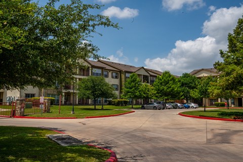 A sunny day at the apartment complex with cars parked in the driveway.