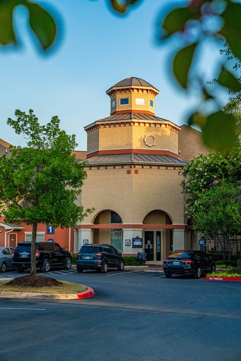 A building with a round tower and a parking lot in front.