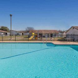 a large swimming pool with a fence and houses in the background