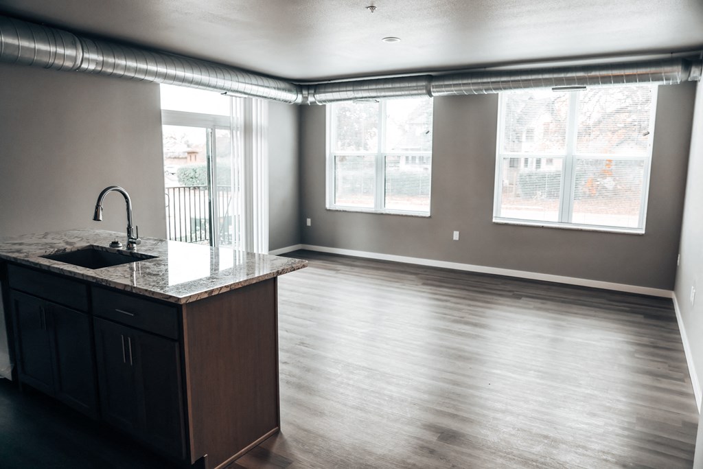 an empty living room with a kitchen and a large window