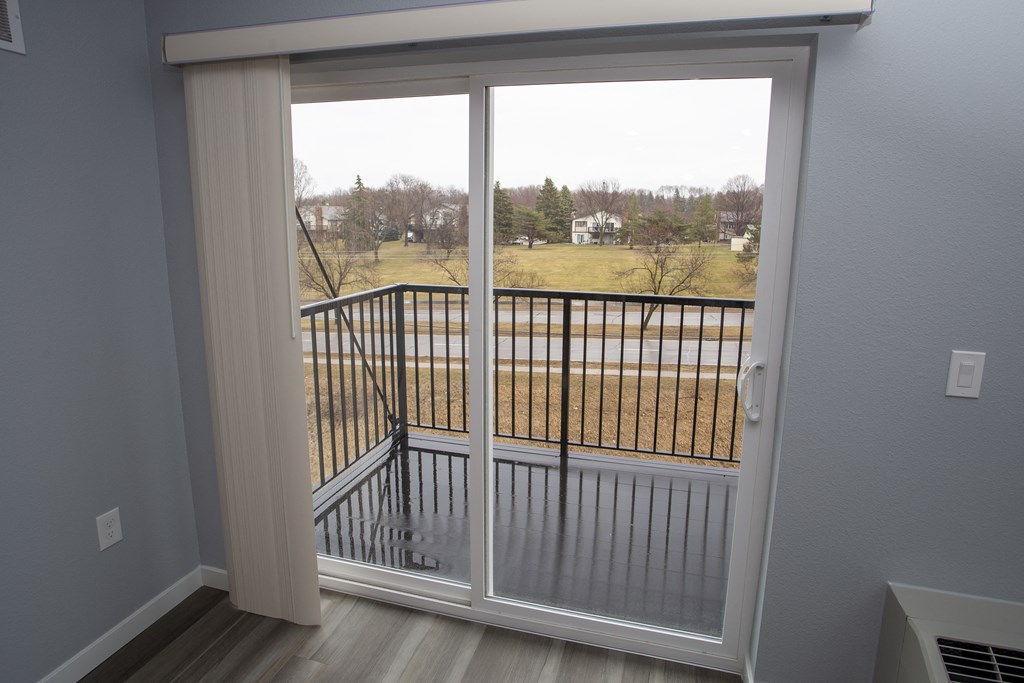 a sliding glass door leading to a balcony with a view of a field
