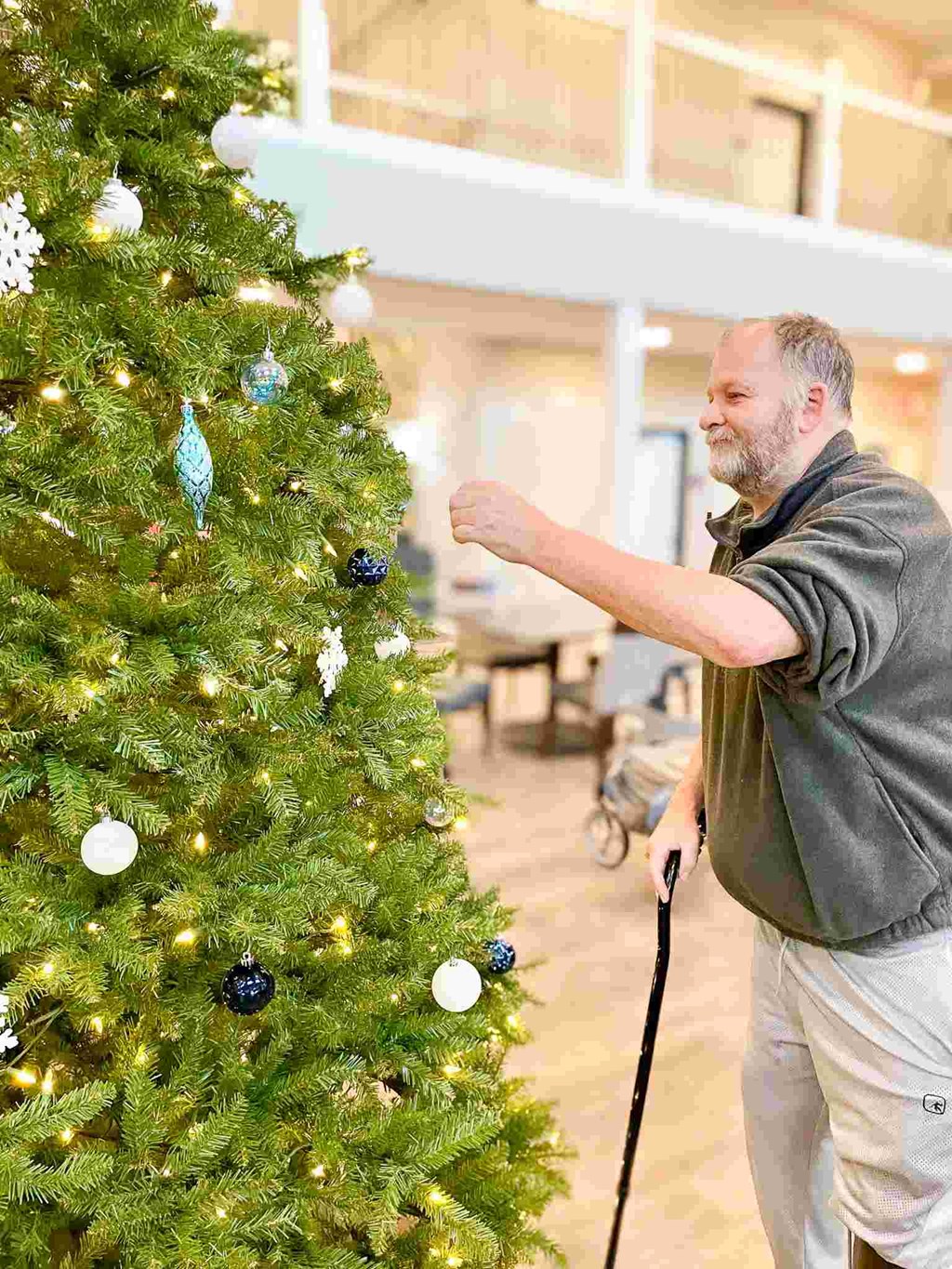 a man with a cane standing next to a christmas tree