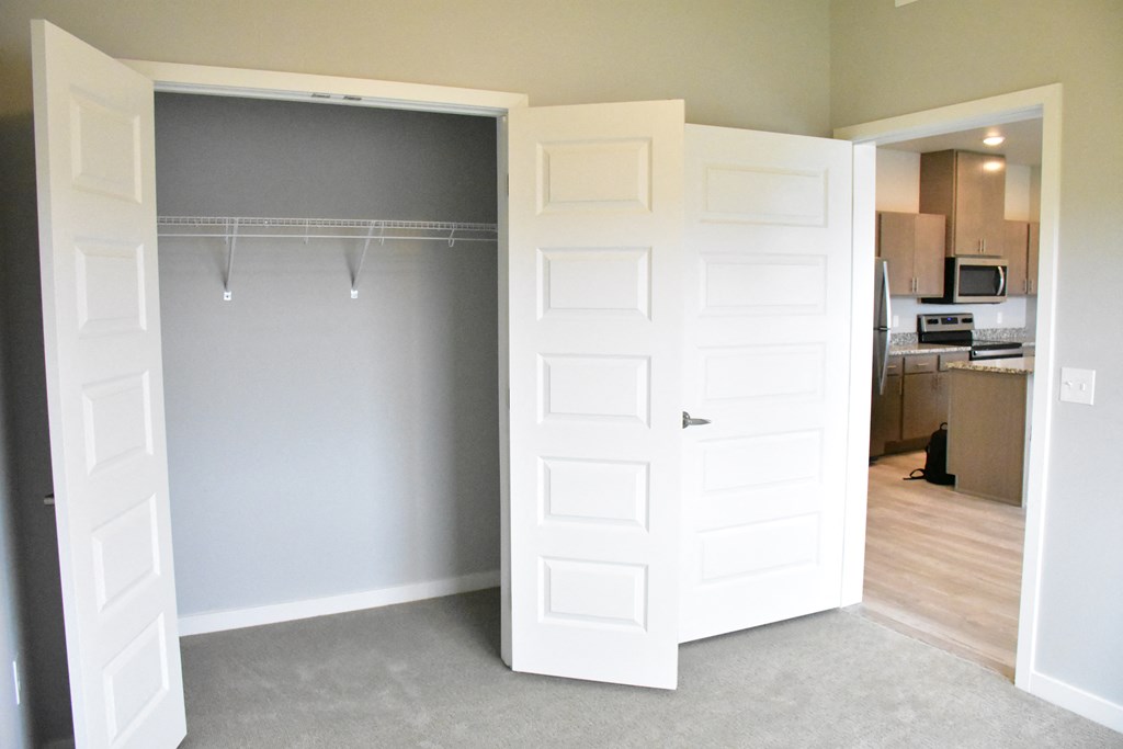 an open closet in a living room with a door open to a kitchen