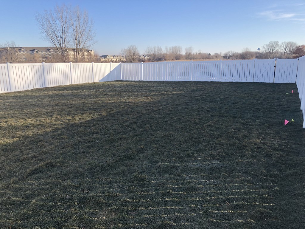 a backyard with a white fence and a green lawn with a pink ball