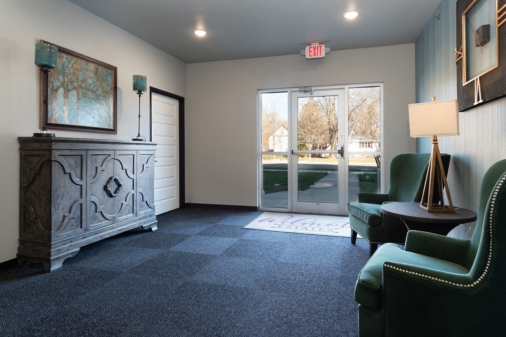a living room with green chairs and a fireplace and glass doors