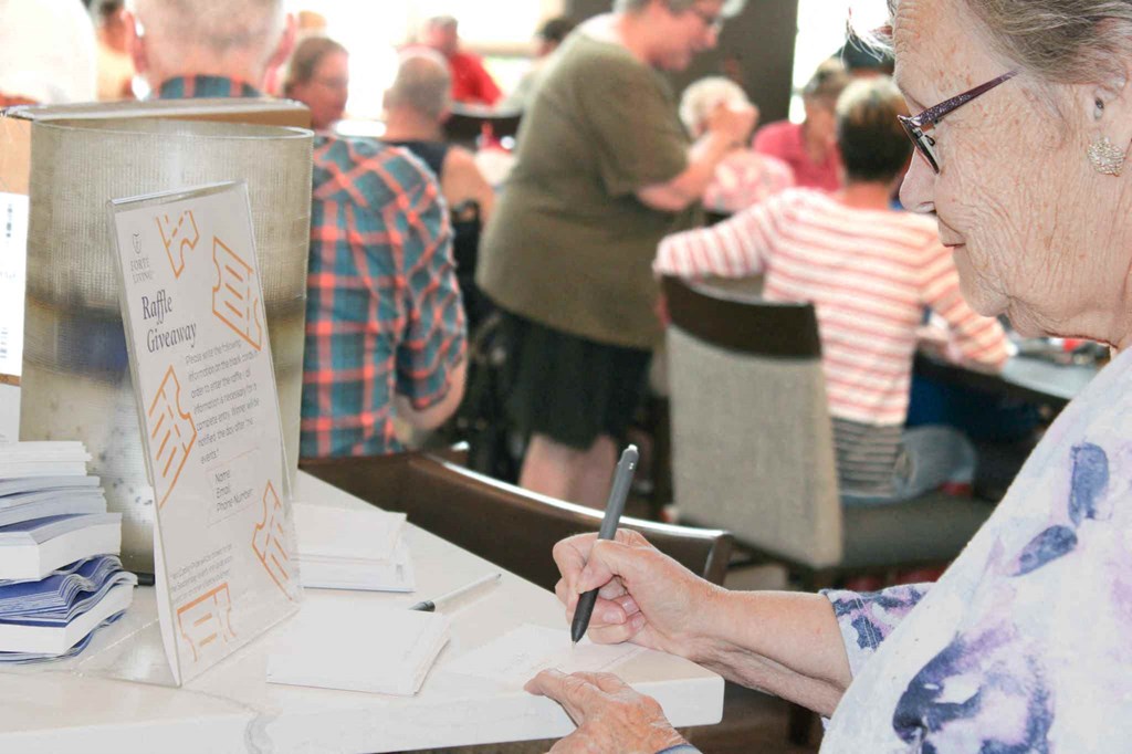 an older woman sitting at a table writing on a piece of paper