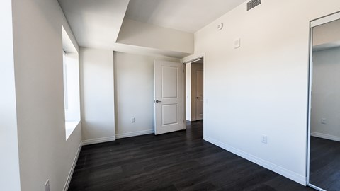 A spacious room with white walls and dark wood flooring.