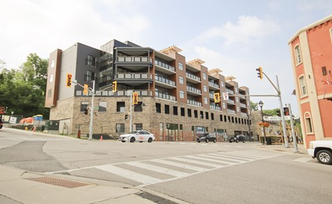 A modern building with a mix of brick and panel construction is situated on a street corner with a crosswalk in front.