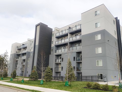 A large grey apartment building with balconies and trees in front.