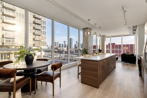 A modern kitchen with a dining table and chairs in front of a large window overlooking a cityscape.