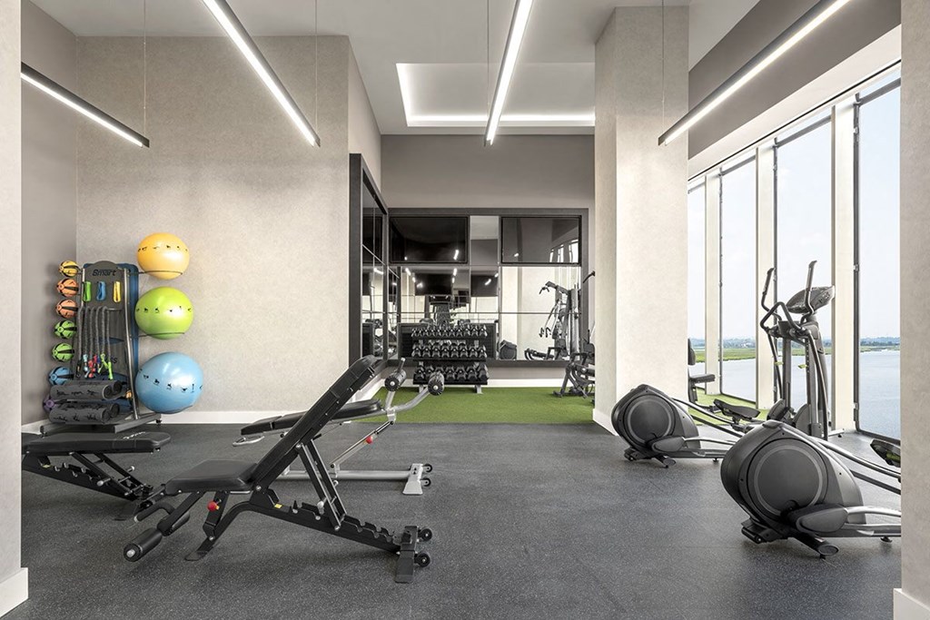 Interior photo of the gym at RVR showing an elliptical facing out the large windows with a view of the water, as well as various strength training areas.