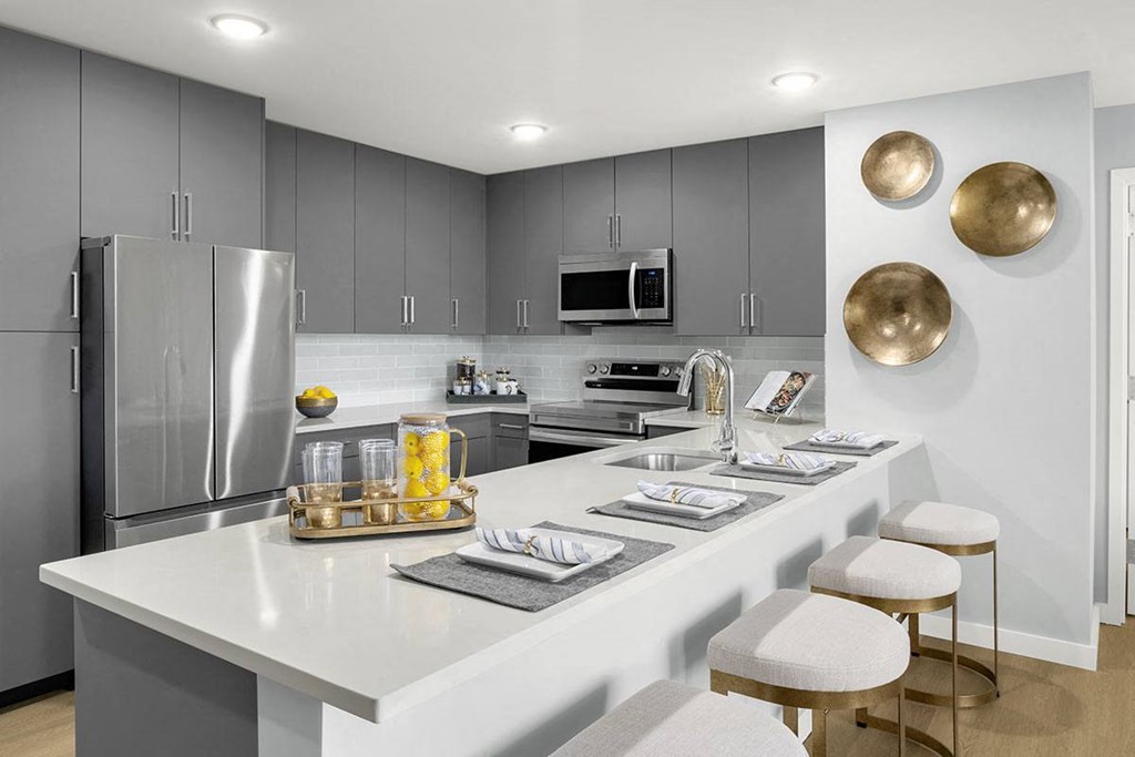 Interior photo showing a typical kitchen in an apartment at RVR, featuring Luxury Vinyl plank flooring,. Modern gray cabinetry, stainless steel appliances and white quarts countertops.